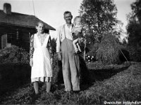 Image21  Roosa (kutsumanimi Ruusa) Huusko (o.s. Syrjälä, 2.5.1889 - 20.3.1964) ja aviomiehensä Timo Huusko  (8.5.1888 - 22.6.1981) sylissään tyttärenpoikansa Seppo Ilmonen (s. 12.4.1952) seisovat Killilän pihalla, takana vanha talo